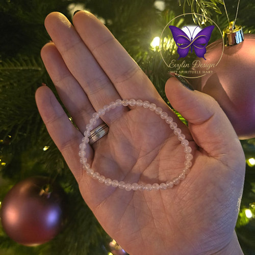 Rozenkwarts armband 4 mm met fijne kralen liggend in de hand, met sfeerverlichting en kerstdecoratie op de achtergrond